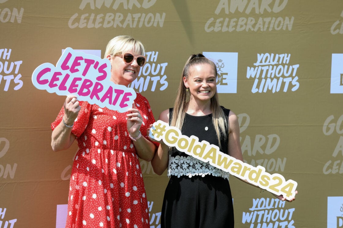 The image shows two women smiling and posing in front of a backdrop with 